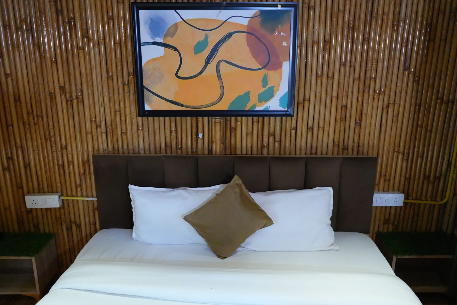 Inside a hut: bamboo walls, a made bed and framed art